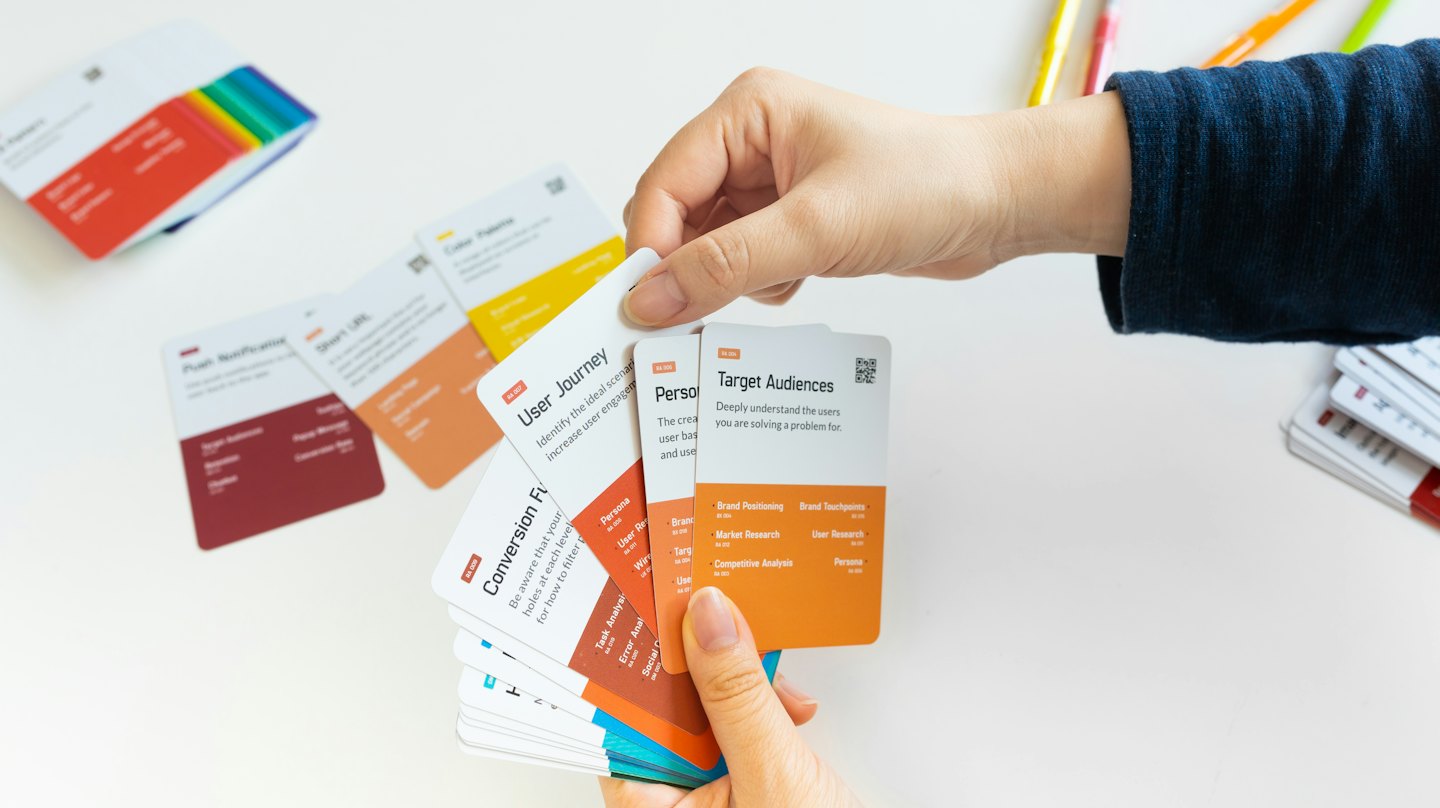 Hands hold a fan of colorful design thinking cards.